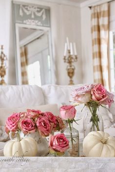 pink roses and pumpkins are in vases on the coffee table