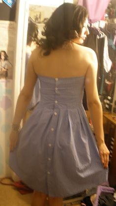 a woman standing in front of a mirror wearing a blue and white dress with buttons