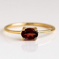 a gold ring with a red stone on it's side, sitting on a white surface