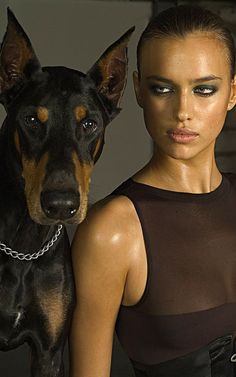 a woman standing next to a black and brown dog with chains on it's neck