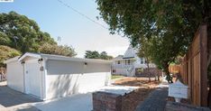 two garages on the side of a street next to a fence and trees in front of a house