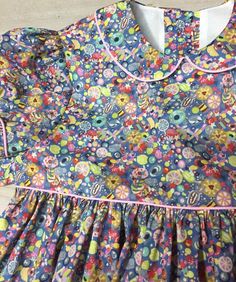 "This is a beautifully made bodice lined party dress made from playful tana Lawn sugar rush blue liberty of London fabric colors include purple/blue, pink, and yellow. It has a Peter Pan collar piped with pink. The dress has puffy sleeves trimmed with pink piping. It has ties that tie in the back into a beautiful bow. The dress buttons in the back. This handcrafted dress has all finished seams and a 3 \" hem. This dress can be customized to have a white collar and or white cuffs on the sleeves. Dress Peter Pan Collar, Puffy Sleeve Dress, Hunter Green Dresses, Candy Dress, Liberty Tana Lawn, Rush Dresses, Liberty Of London Fabric, Dress Buttons, Lawn Fabric