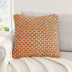 an orange and white pillow sitting on top of a gray couch next to a window