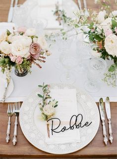 the table is set with white and pink flowers, silverware, and napkins