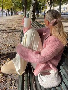 two women sitting on a park bench drinking coffee