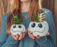 a woman holding two plants with faces painted on them