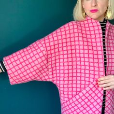 a woman with blonde hair wearing a pink and black checkered top, standing against a blue wall