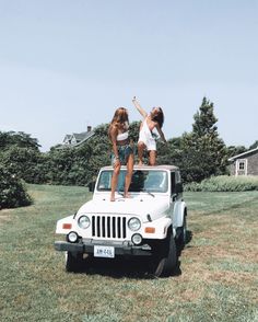 two girls standing on top of a white jeep