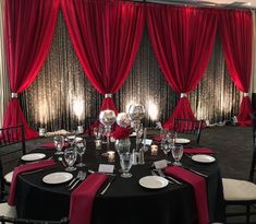 a black table topped with white plates and silverware next to red curtained walls