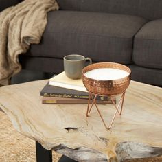 a wooden table topped with a metal bowl and coffee cup on top of it next to a couch