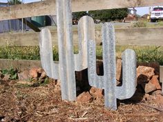 a metal cactus sitting on top of a pile of rocks next to a wooden fence