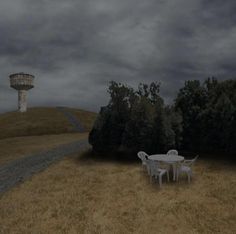 a table and chairs sitting on top of a grass covered field next to a water tower