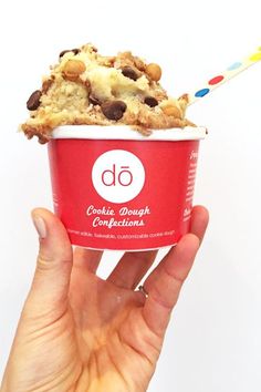 a hand holding an ice cream sundae with chocolate chip cookies on top