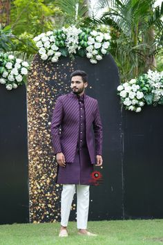 a man standing in front of a black fence wearing a purple jacket and white pants