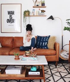 a woman sitting on top of a brown couch in a living room next to a coffee table