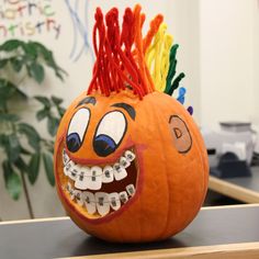 an orange pumpkin decorated with teeth and rainbow hair