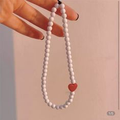 a woman's hand holding a white beaded necklace with a red heart on it