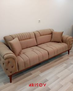 a tan couch sitting on top of a hard wood floor next to a white wall