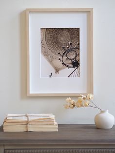 a white vase sitting on top of a wooden table next to a framed photo and books