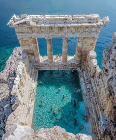 people are swimming in the blue water at an ancient temple near the sea, surrounded by rocky cliffs