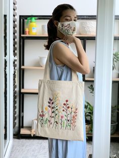 a woman wearing a face mask standing in front of a book shelf holding a tote bag