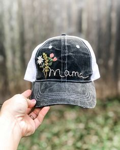 a person holding up a hat with flowers on it that says, mama written in cursive writing