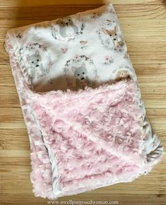 a pink and white blanket laying on top of a wooden floor next to a box