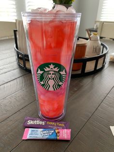 a pink drink in a plastic cup on a table next to a package of candy