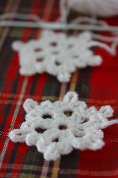 two crocheted snowflakes sitting on top of a red plaid table cloth