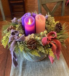 two candles are sitting in a bowl with greenery and pine cones on the table