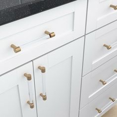 a kitchen with white cabinets and black counter tops, gold pulls on the handles are brass