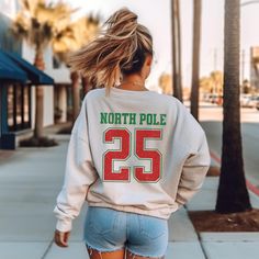 Channel your inner Santa with this retro varsity-style Christmas sweatshirt. Featuring a classic Santa Claus graphic on the front chest pocket and a bold "North Pole 25" on the back, this sweatshirt is a festive twist on a timeless design. Perfect for spreading holiday cheer, whether you're attending a Christmas party or simply enjoying a cozy night in. Crafted from premium materials for maximum comfort and durability, this sweatshirt is a must-have for the season.  - Unisex sizing  - Fits true Winter Varsity Tops With Letter Print, Winter Varsity Top With Letter Print, Varsity Style Letter Print Top For Winter, Varsity Letter Print Top For Winter, Varsity Style Winter Top With Lettering, Winter College Tops With Lettering, Varsity Style Top With Lettering, Lettering Tops For College In Winter, Santa Sweatshirt