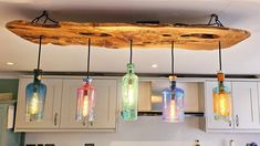 three glass bottles hanging from a wooden beam in a kitchen with white cabinets and drawers