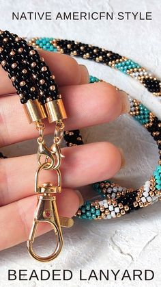 the beaded lanyard is being held up by someone's hand with two gold clasps