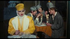 a group of women sitting at a table with drinks in front of them and one woman standing next to her