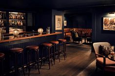 a dimly lit bar with stools and wooden tables in the corner, along with pictures on the wall