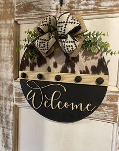 a welcome sign hanging on a door with a bow and some greenery in front of it