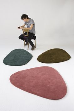 a man sitting on a chair in front of four different colored rugs that are shaped like shapes