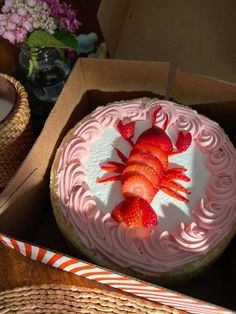 there is a cake with strawberries on it in the box next to some flowers