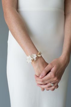 a woman in a white dress holding her hands together with flowers on the wrist and bracelet