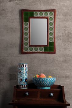 a bowl of fruit sitting on top of a table next to a mirror and vase