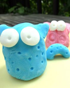 three blue, pink and white cookies with googly eyes sitting on a yellow table