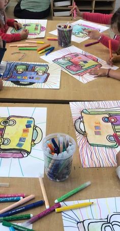 two children sitting at a table drawing with crayons on paper and colored pencils