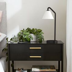 a bedside table with books and plants on it next to a bed in a bedroom