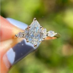 a close up of a person's hand holding a ring with a pear shaped diamond