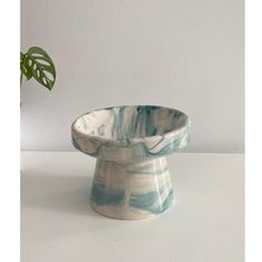 a white and blue bowl sitting on top of a table next to a green plant