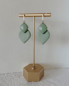 two green heart shaped earrings hanging from hooks on a wooden stand in front of a white wall