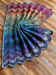 a multicolored crocheted blanket laying on top of a hard wood floor