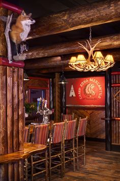 a wooden table and chairs in a room with wood beams on the ceiling, an antelope sculpture hanging from the ceiling