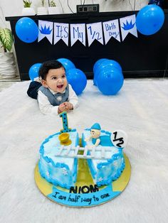 a young boy sitting in front of a blue and yellow cake with the number one on it